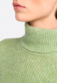 Hellgrüner Strickrollkragenpullover mit gerippter Textur und hohem Kragen, ausgestattet mit weichen Fasern und einem leicht fuzzy Aussehen.