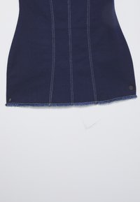 Jeans obleka v temno modri barvi z kontrastnim belim šivanjem, strukturirana oblika, razfrkan rob in majhna črna kovinska podrobnost na spodnjem robu.
