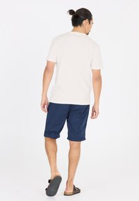 Valkoinen lyhythihainen t-paita yhdistettynä tummansinisiin sortseihin. Rennon tyyppinen, puuvillamateriaali ja yksinkertainen muotoilu, sortseissa käännetyt hihansuut.