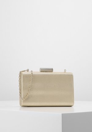 Prostokątna złota kopertówka o teksturowanej powierzchni i srebrzystym zapięciu, z delikatnym łańcuszkiem, na białym postumencie.