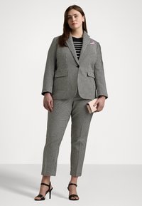 Black and white houndstooth suit with a blazer and slim-fit pants, paired with a black and white striped top and a pink-accented pocket square.