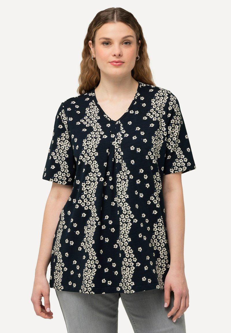 Námořnický top s krátkým rukávem a véčkovým výstřihem, s bílým květinovým vzorem a skládáním v přední části pro přidanou texturu.