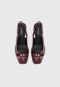 Scarpe slingback in pelle bordeaux con punta quadrata, decorate con dettagli in metallo argentato e accenti circolari, con una chiusura a fibbia nella parte anteriore.