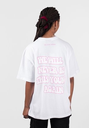 Persona con cabello trenzado atado con una goma roja, que viste una camiseta blanca que dice "NUNCA VOLVEREMOS A SER TAN JÓVENES" en letras rosas.