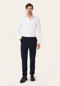 Witte blouse met lange mouwen, een puntige kraag en een knoopsluiting aan de voorkant, gecombineerd met navy tailor made broek en zwarte veterschoenen.