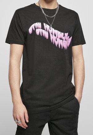 T-shirt noir en coton, avec un motif graphique rose affichant le texte "RESTE HUMBLE RESTE AFFAMÉ" en police audacieuse et déformée.