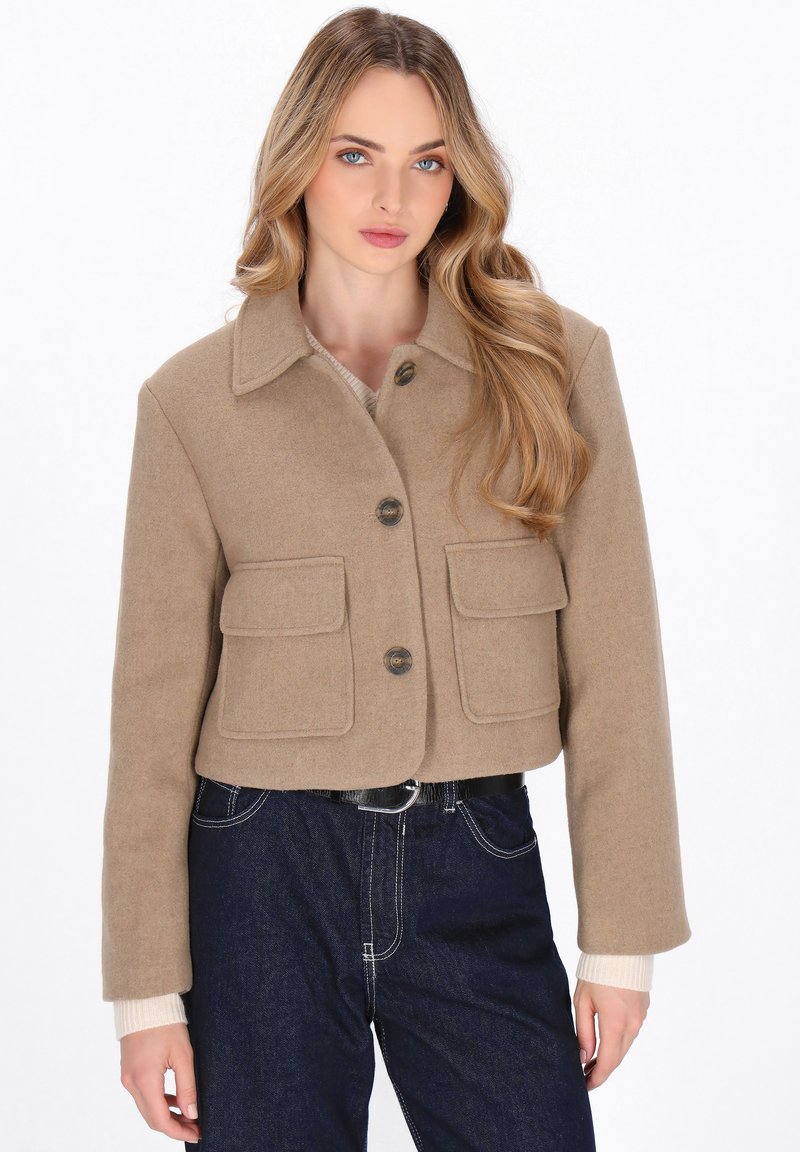 Giacca in lana beige tagliata con due tasche frontali, grandi bottoni e colletto a punta, abbinata a pantaloni in denim scuro.