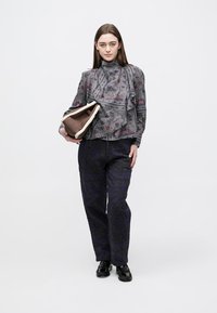 Γκρι μπλούζα με σχέδιο και βολάν στο λαιμό, συνδυασμένη με παντελόνι σκούρου μπλε με υφή. Το μοντέλο κρατά καφέ και κρεμ τσάντα. Μαύρα παπούτσια.
