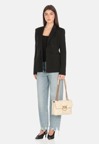 Blazer nero doppiopetto con rever arrotondati, indossato su una maglietta nera, abbinato a jeans chiari strappati e scarpe nere a punta, mentre porta una borsa color crema.