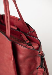 Borsa a tracolla in pelle rossa con doppi manici, tasca con zip visibile, bordi neri e chiusura in metallo per il fissaggio della tracolla.