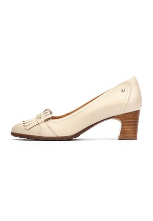Zapato de tacón de piel color beige con punta redondeada, detalle de borlas en el empeine y tacón de madera marrón texturizada. Superficie lisa y diseño sencillo.