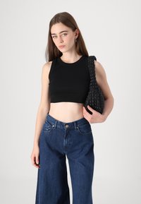 Musta ribattuva lyhyt toppi, leveät siniset farkut ja teksturoitu musta olkalaukku. Yksinkertainen muotoilu, joka on istuva ja rento.