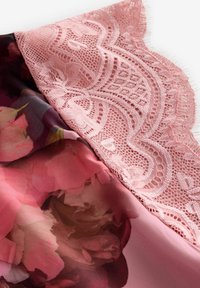 Priehľadná látka s kvetinovým vzorom v odtieňoch ružovej, s ozdobným krajkovým okrajom v tvare vala. Hladká textúra a jemný dizajn.