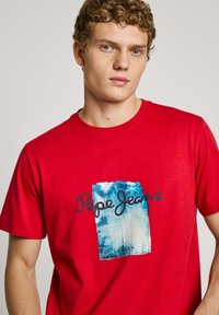 Red cotton T-shirt featuring a blue and white graphic print with the text "Pepe Jeans" and "London." Classic crew neckline and short sleeves.