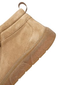 Lysebrun ruskindsankelstøvle med tyk, struktureret gummisål og trækkehempe bagpå for nem påtagning.