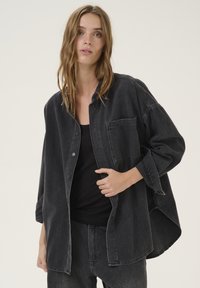 Black denim overshirt with a relaxed fit, featuring a button-up front, chest pocket, and dropped shoulders. Soft texture and casual design.