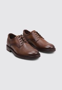 Zapatos de vestir de cuero marrón con una textura suave, punta redondeada y cordones de seis ojales. Suela marrón resistente, con un detalle de costura sutil.
