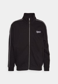 Veste noire zippée en tissu lisse, avec un col montant, deux poches latérales et des bandes blanches le long des épaules. "Tigers" est brodé en blanc.