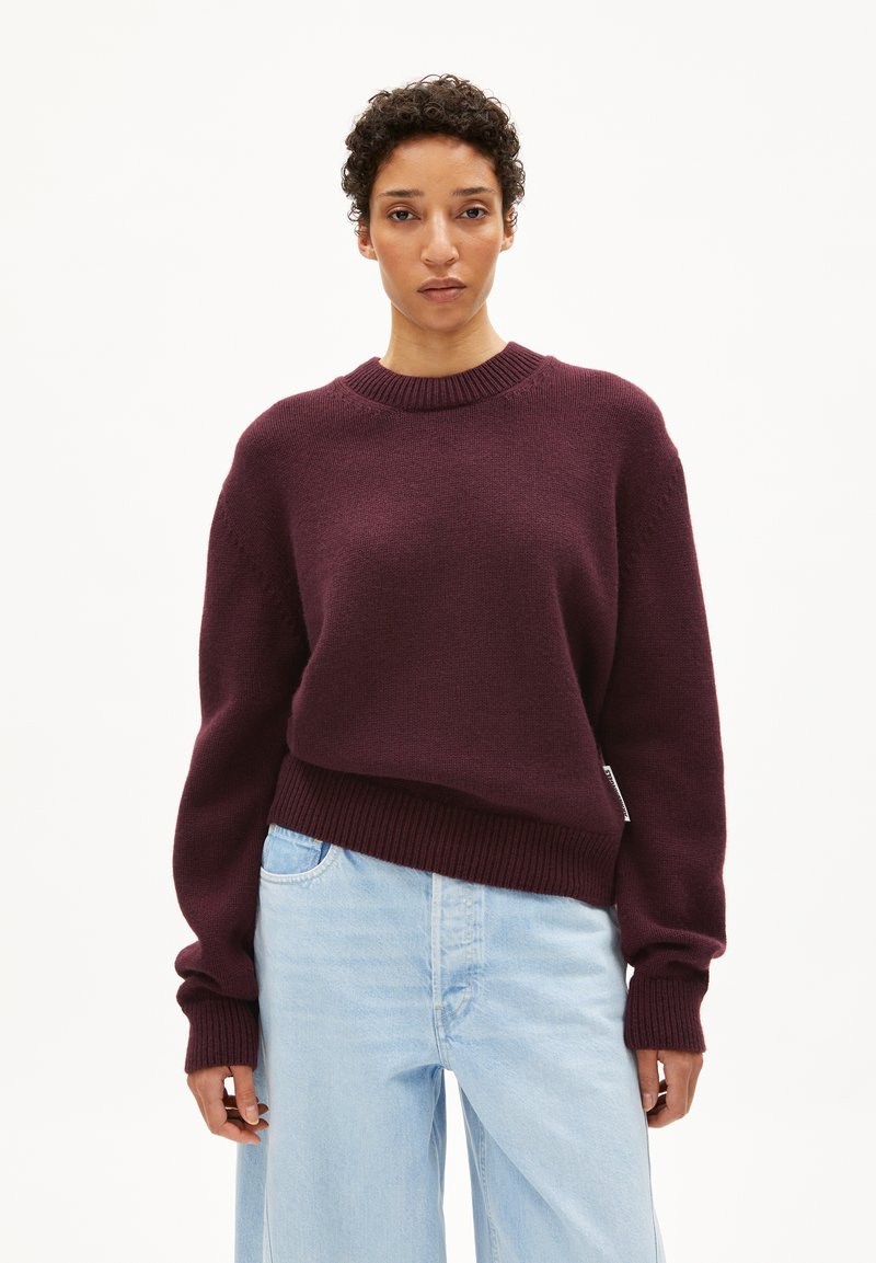 Bordeaux gebreide trui met een geribde halslijn en manchetten, met een relaxte pasvorm en zijsplitdetail, gecombineerd met lichtblauwe wijde jeans.