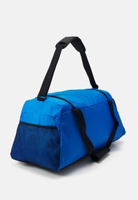Sac de sport bleu avec poignées noires, de forme rectangulaire, en tissu lisse, doté d'une poche en maille sur un côté. Fermeture éclair sur le dessus.