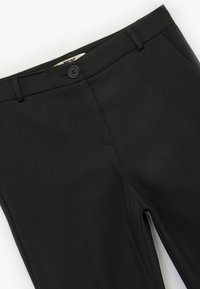 Pantalones negros de tejido suave, con cierre de botón, cremallera y bolsillos delanteros. Diseño de pierna recta sin patrones visibles.