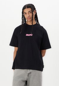 Black cotton t-shirt with short sleeves; features pink "CULTIVATE GROWTH" text centered on the chest; relaxed fit design.