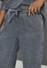 Grå denim joggers med elastisk talje og snøre, sidelommer og en blød, struktureret overflade.