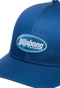 Blaue Baseballmütze aus strukturiertem Stoff, mit einem gestickten Billabong-Logo in Hellblau innerhalb eines ovalen Designs auf der Vorderseite.