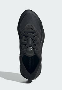 Černá atletická sneaker se strukturálním svrškem, zaoblenou špičkou, šněrovacím designem a akcenty s logem. Podešev má výrazný vzor drážkování.