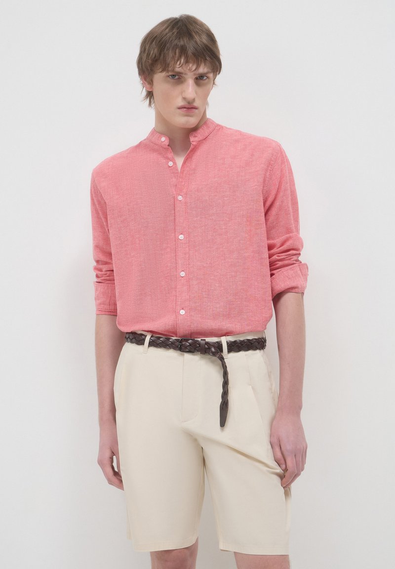 Camicia leggera in corallo con texture, colletto alla coreana, abbinata a pantaloni corti crema su misura e una cintura in pelle intrecciata.