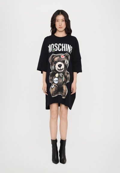 Rochie t-shirt supradimensionată, de culoare neagră, cu un grafic cu un urs, insigne colorate și logo-ul "Moschino" în partea de sus. Material din bumbac neted.
