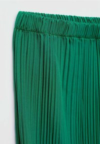 Groene geplooide stof met een zachte textuur en een elastische tailleband. Het materiaal lijkt licht en luchtig, waardoor verticale lijnen in het ontwerp ontstaan.