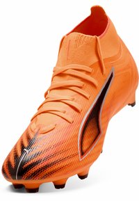 Lys orange fodboldstøvle med en struktureret overdel, slank design, snørebånd og et sort accentmønster. Har formede studs for trækkraft.
