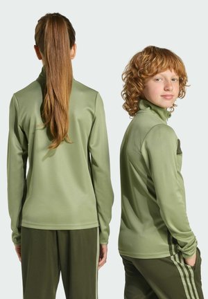Two individuals wearing matching olive green athletic zip-up tops and pants. The fabric appears smooth with a slight sheen.