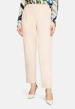 Beżowe, dopasowane spodnie o gładkiej fakturze, z luźnym krojem, plisami z przodu i podwiniętymi mankietami. Noszone z białymi szpilkami.