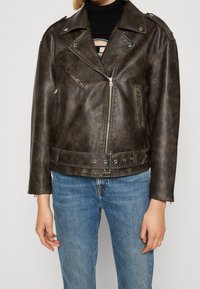 Veste de moto en faux cuir marron avec zip argenté, fermetures à pression et taille ceinturée. Comprend des poches zippées et des revers structurés.