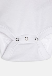 Hvit bomullsbody med trykknapper nederst. Myk tekstur med tettsittende ermer og rund hals. Enkel design.