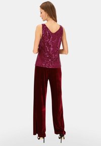 Bordowy top z cekinami, z dekoltem w kształcie litery V i bez rękawów, zestawiony z wysokim stanem i szerokimi spodniami z aksamitu w dopasowanym kolorze.