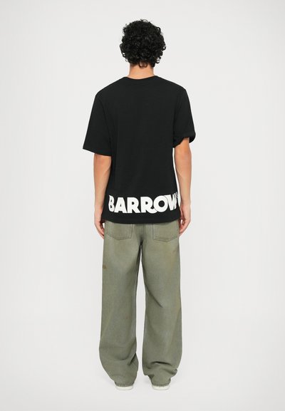 Svart t-skjorte med korte ermer som har stor hvit "BARROWS" tekst på ryggen, kombinert med løstsittende olivengrønne bukser.