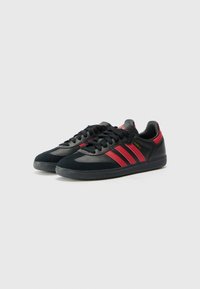 Black and red athletic sneakers with three red stripes, suede and synthetic material, textured rubber sole, round toe, flat laces.