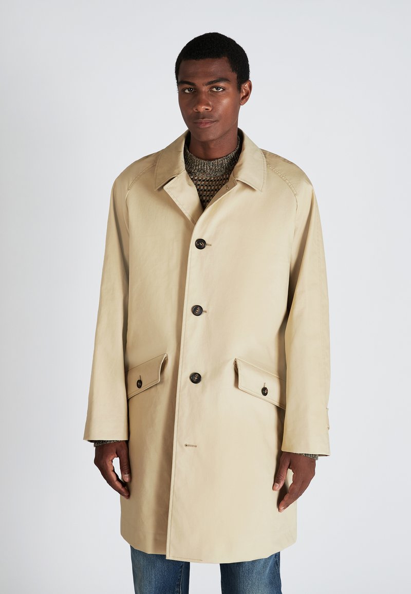 Trench-coat léger beige avec un col cranté, quatre boutons sur le devant, poches latérales et coupe décontractée. Tissu texturé avec une finition lisse.