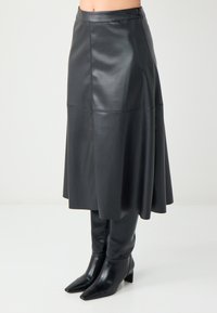 Zwarte leren midi-rok met een uitlopende zoom, gekenmerkt door een gladde textuur en een aansluitende tailleband. Gecombineerd met zwarte kniehoge laarzen met een spitse neus.