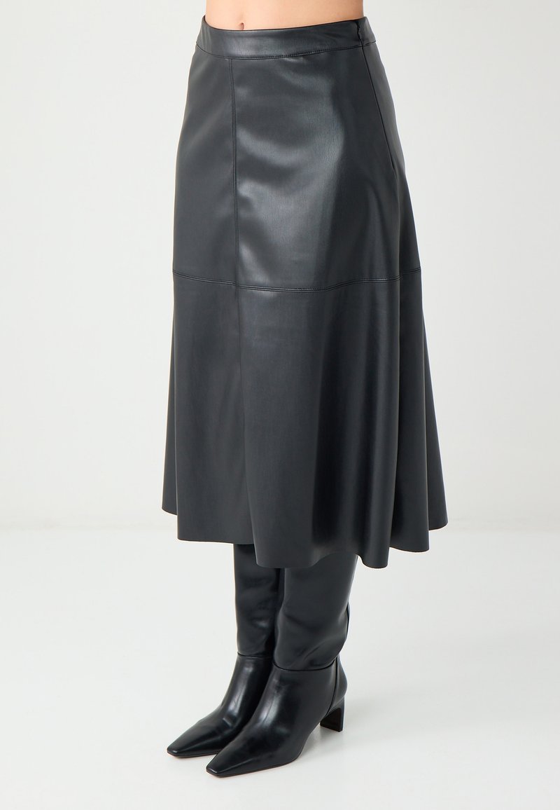 Zwarte leren midi-rok met een uitlopende zoom, gekenmerkt door een gladde textuur en een aansluitende tailleband. Gecombineerd met zwarte kniehoge laarzen met een spitse neus.