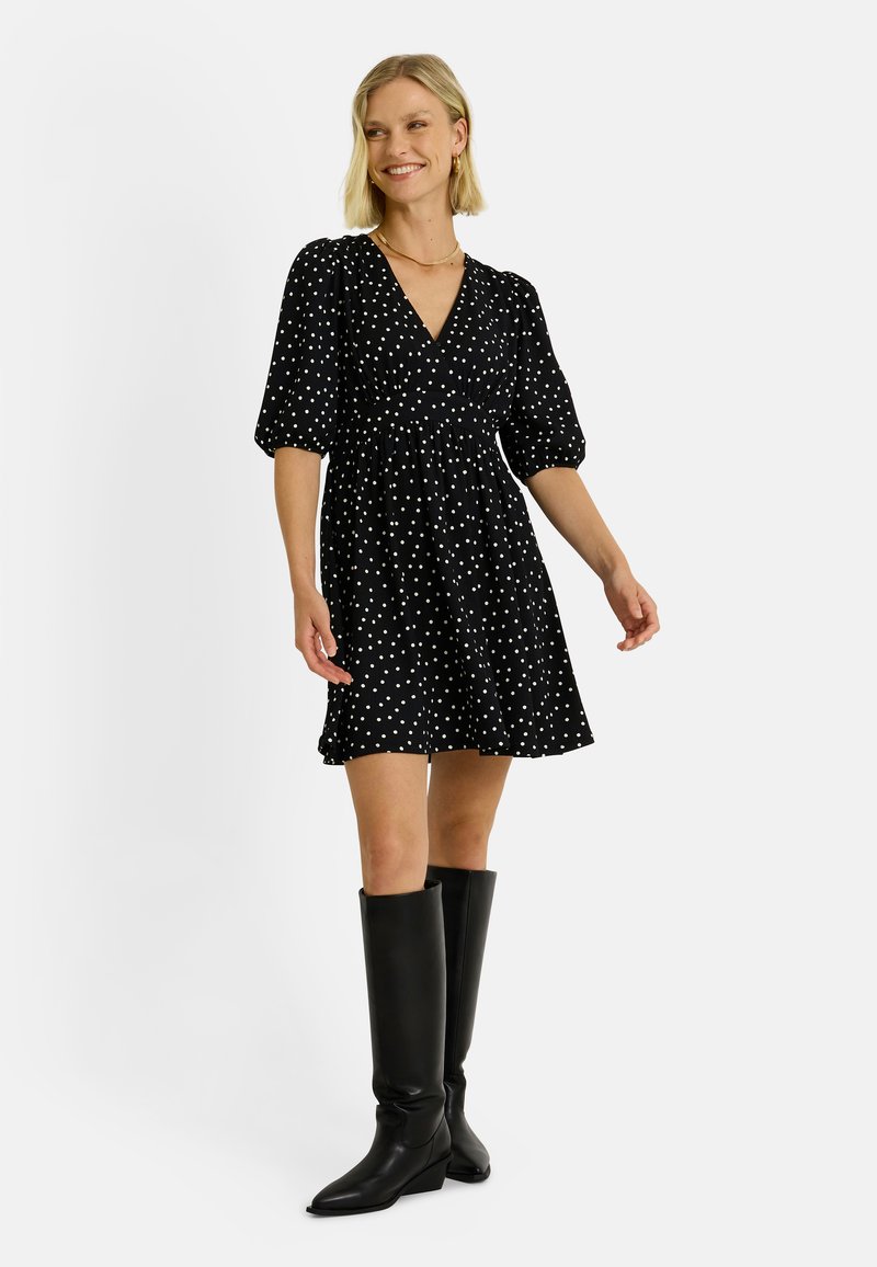 Vestido negro con lunares, con escote en V, mangas abullonadas y falda acampanada, combinado con botas de cuero negras hasta la rodilla.