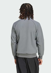 Szary sportowy żakiet o gładkiej fakturze, z prążkowanymi mankietami i dołem, raglanowymi rękawami i dopasowanym krojem. Widok z tyłu nie pokazuje widocznych logo.