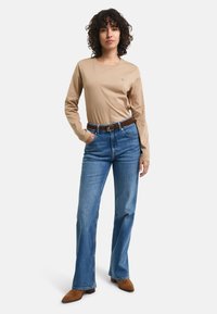 Beige Langarmoberteil, kombiniert mit hellblauen geraden Jeans, braunem Gürtel und braunen Wildleder-Stiefeletten. Lässiges Outfit mit schlichtem Design.