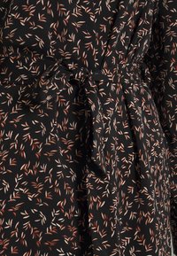Abito in tessuto nero con un motivo floreale in beige e arancio bruciato. Presenta una cintura annodata in vita e una texture morbida e fluida.