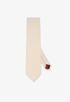 Beżowy krawat z teksturowanym wzorem. Ma zwężany koniec i metkę z czerwonymi oraz granatowymi akcentami. Gładka, elegancka tkanina.
