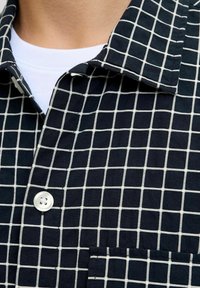Camicia blu navy con motivo a griglia bianca, colletto classico e tasca frontale. Realizzata in un tessuto strutturato.