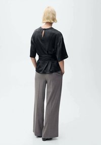 Haut en satin noir à manches courtes avec une ouverture en forme de serrure dans le dos, associé à un pantalon gris à jambes larges en tissu texturé.